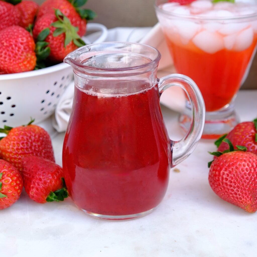 Simple syrup made with strawberries in a small clear pitcher.