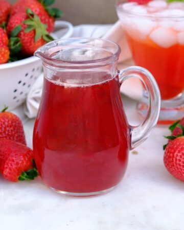 Simple syrup made with strawberries in a small clear pitcher.