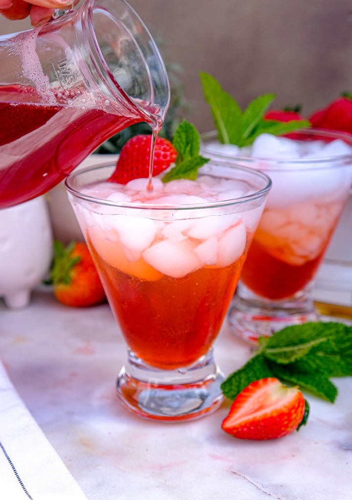 Sparkling water with strawberry syrup with ice being poured in the glass. 