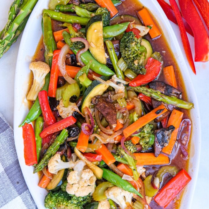 Vegetable stir fry folded in a sauce on a large white serving dish.