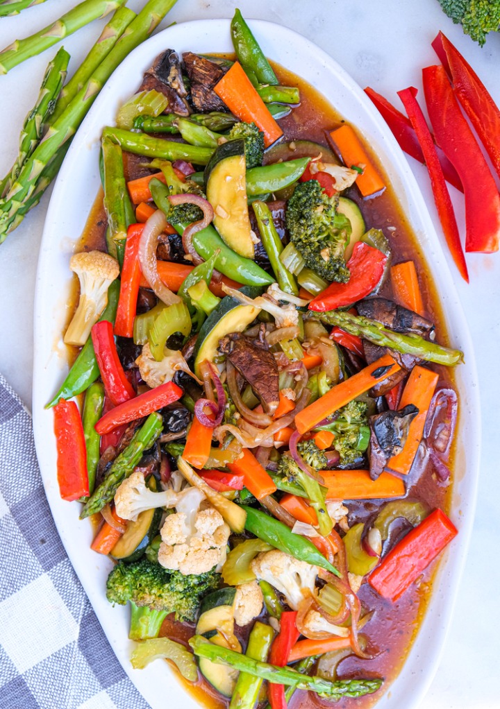 Vegetable stir fry folded in a sauce on a large white serving dish. 