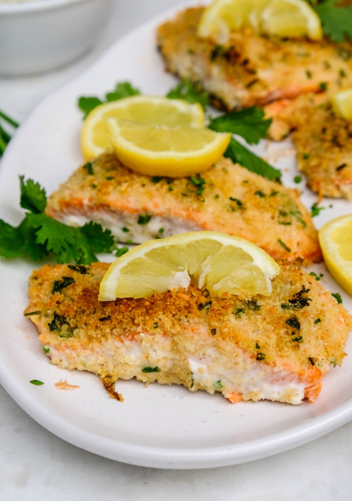 Parmesan crusted salmon slices on a white serving plate with lemon slices. 