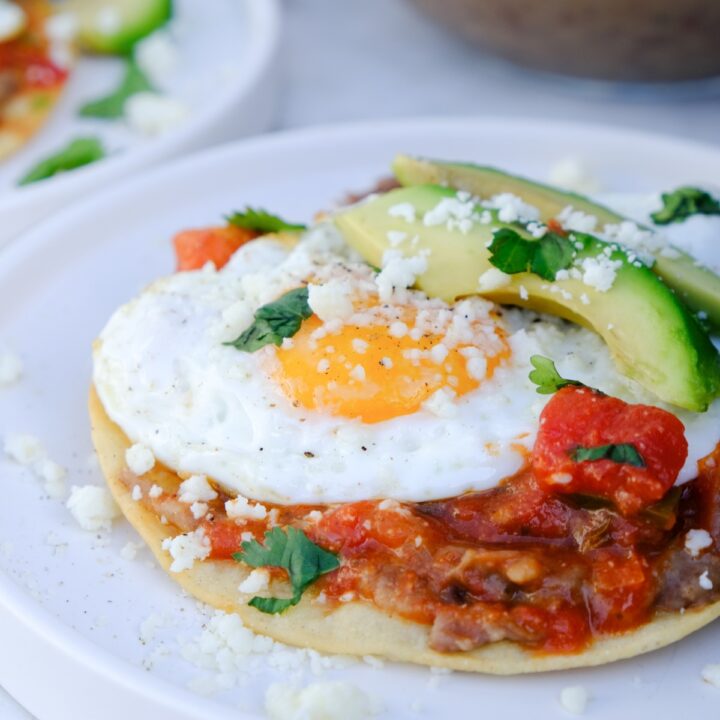 Homemade huevos rancheros with sunny side up egg and sliced avocados on a white plate.