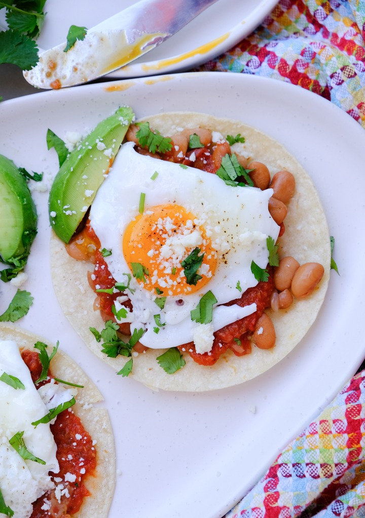 Huevos rancheros with whole beans on a white serving plate. 