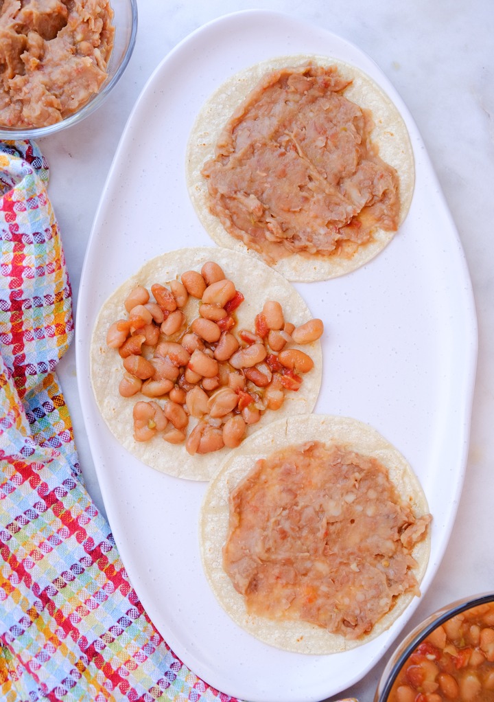 Warm corn tortillas on a platter with whole and refried beans. 