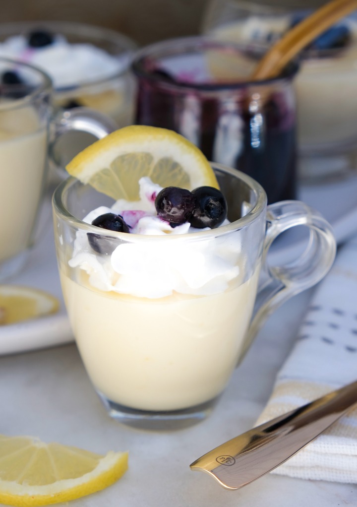Lemon posset in a small glass dish topped with whipped cream and blueberries. 