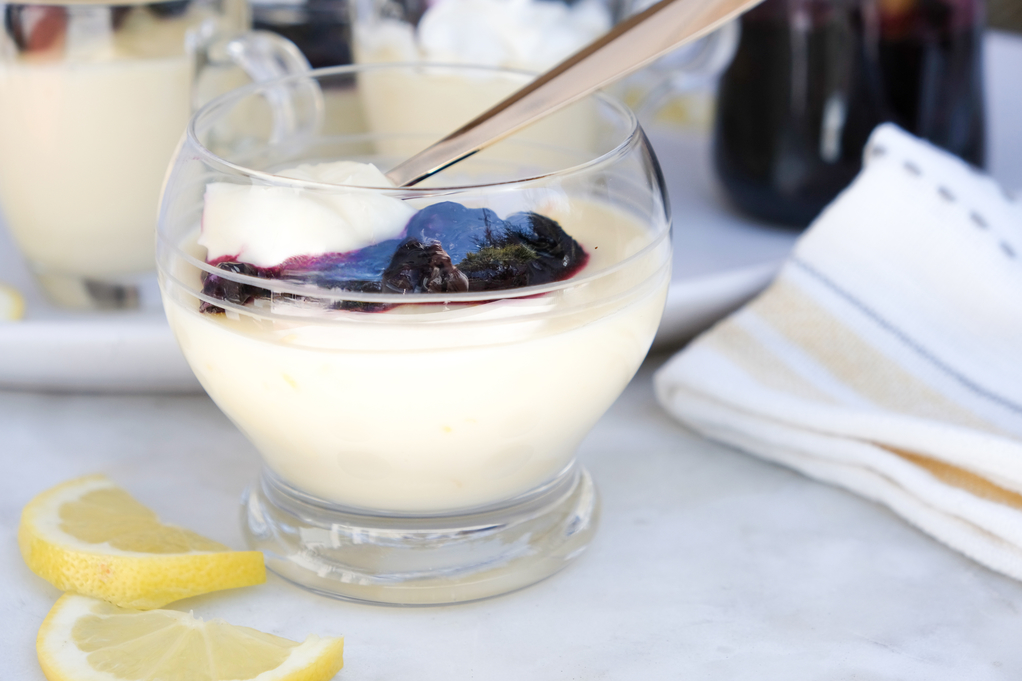 Small glass dish with lemon dessert topped with blueberry sauce. 