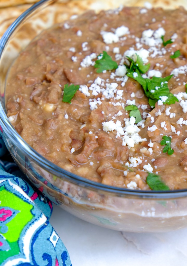 Refried beans with cojita cheese and cilantro in a clear serving bowl. 