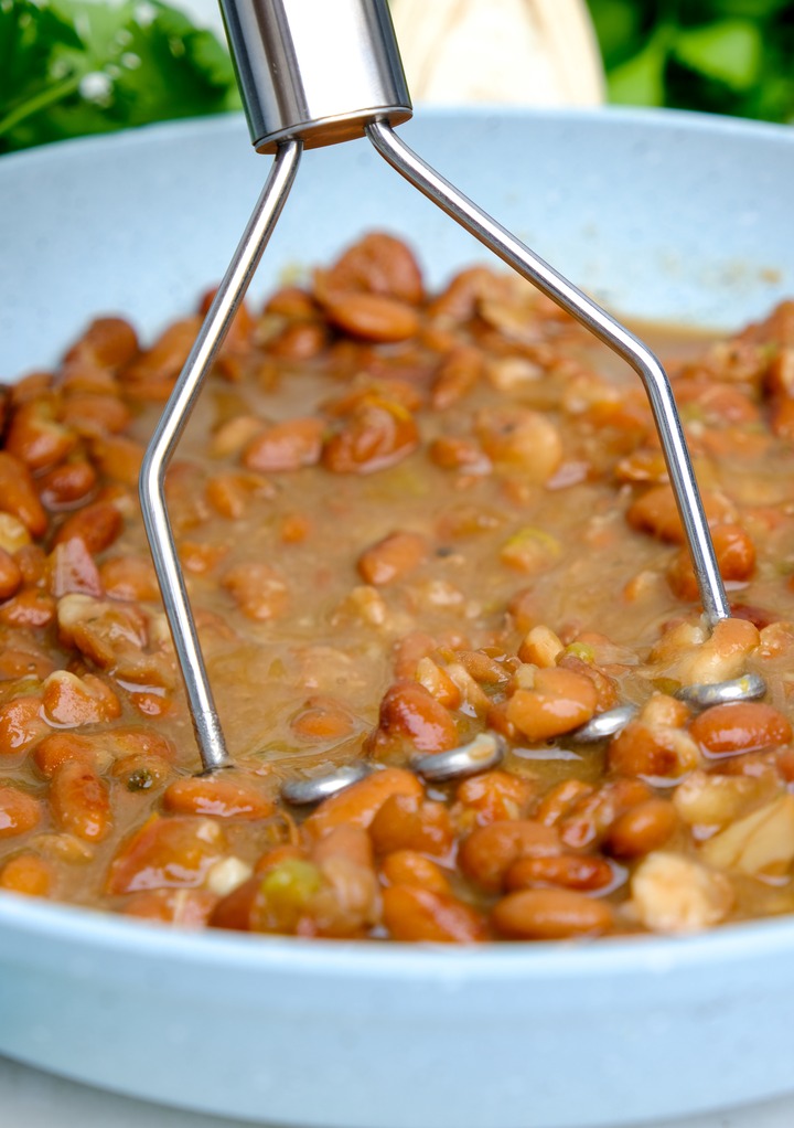 Mashing beans with a potato masher in a skillet. 