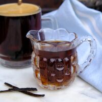 Vanilla syrup in a small pouring pitcher with coffee in the background.