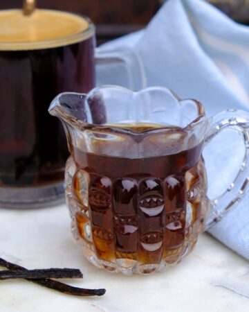 Vanilla syrup in a small pouring pitcher with coffee in the background.