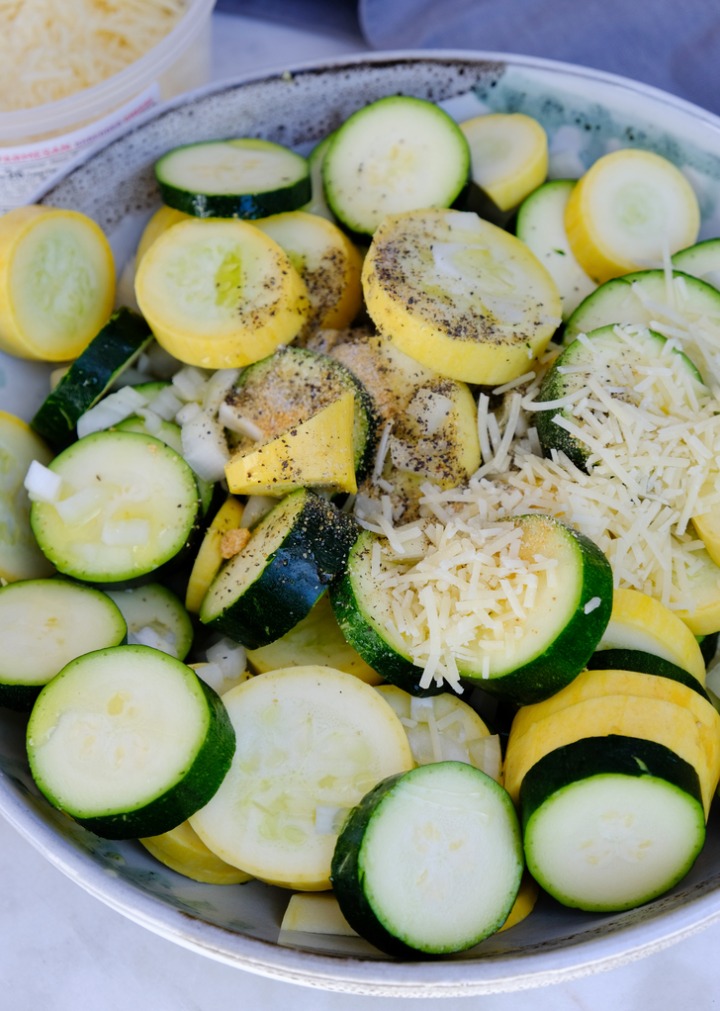 Sliced zucchini in a ceramic bowl with seasoning on top. 