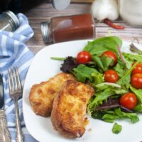 Pork chips with a salad on the side on a white plate.