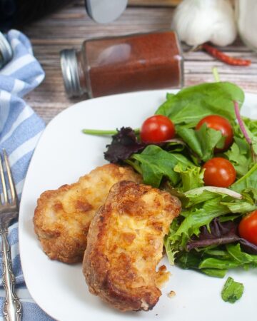 Pork chips with a salad on the side on a white plate.