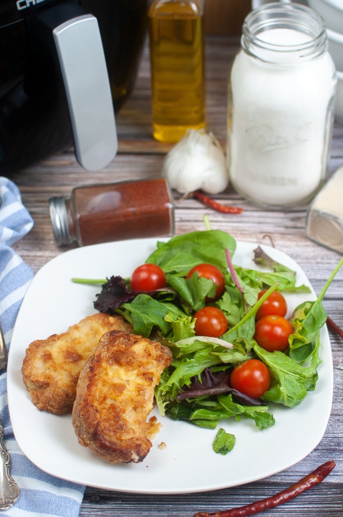 Pork chips on a white plate with a salad on the side. 