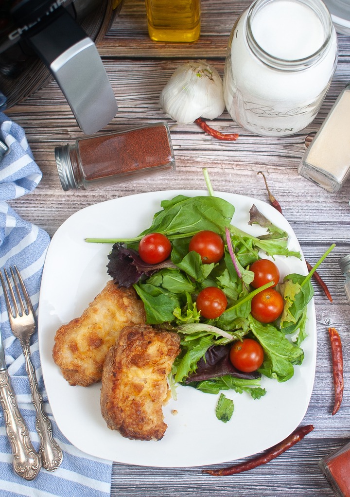 Top view of a dinner plate with pork chops and a green salad with tomatoes. 