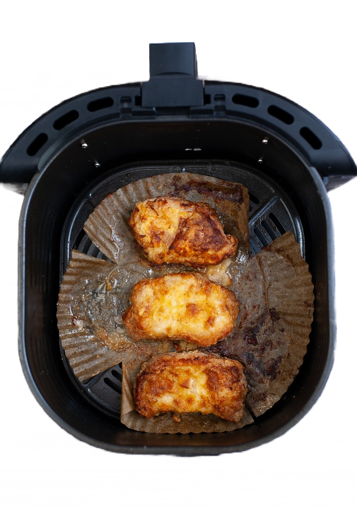 Pork chops in an air fryer basket just cooked golden brown. 