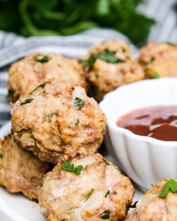 Turkey meatballs cooked in an air fryer on a white serving plate with a side of bbq sauce.