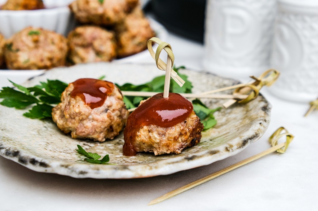 Meatballs topped with a bbq sauce on a small appetizer plate. 