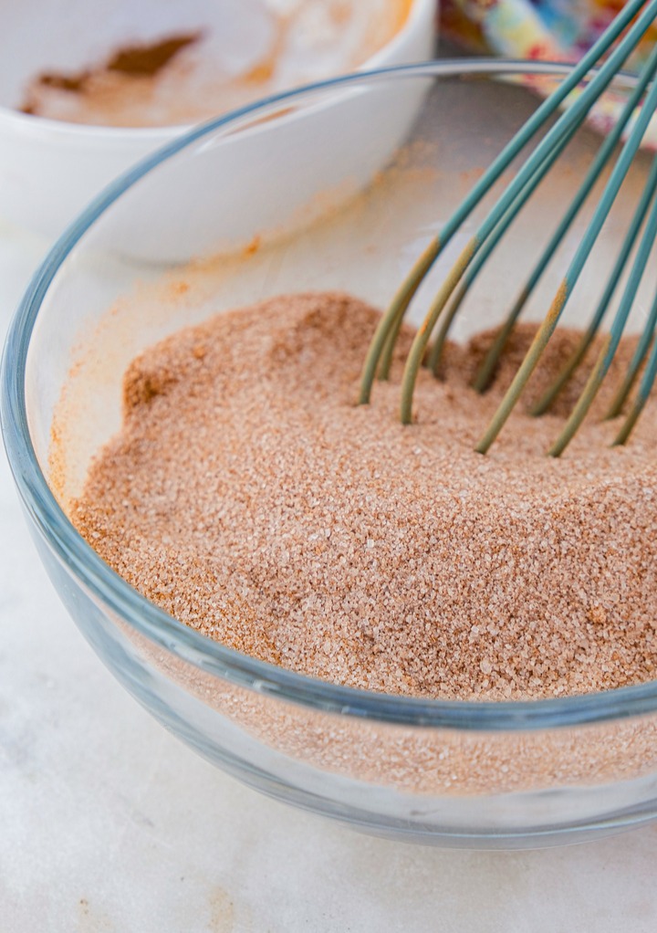 Cinnamon sugar mixture in a clear mixing bowl with a whisk. 