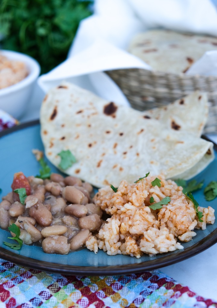 Rice and beans with tortillas on a blue plate with a brown rim. 