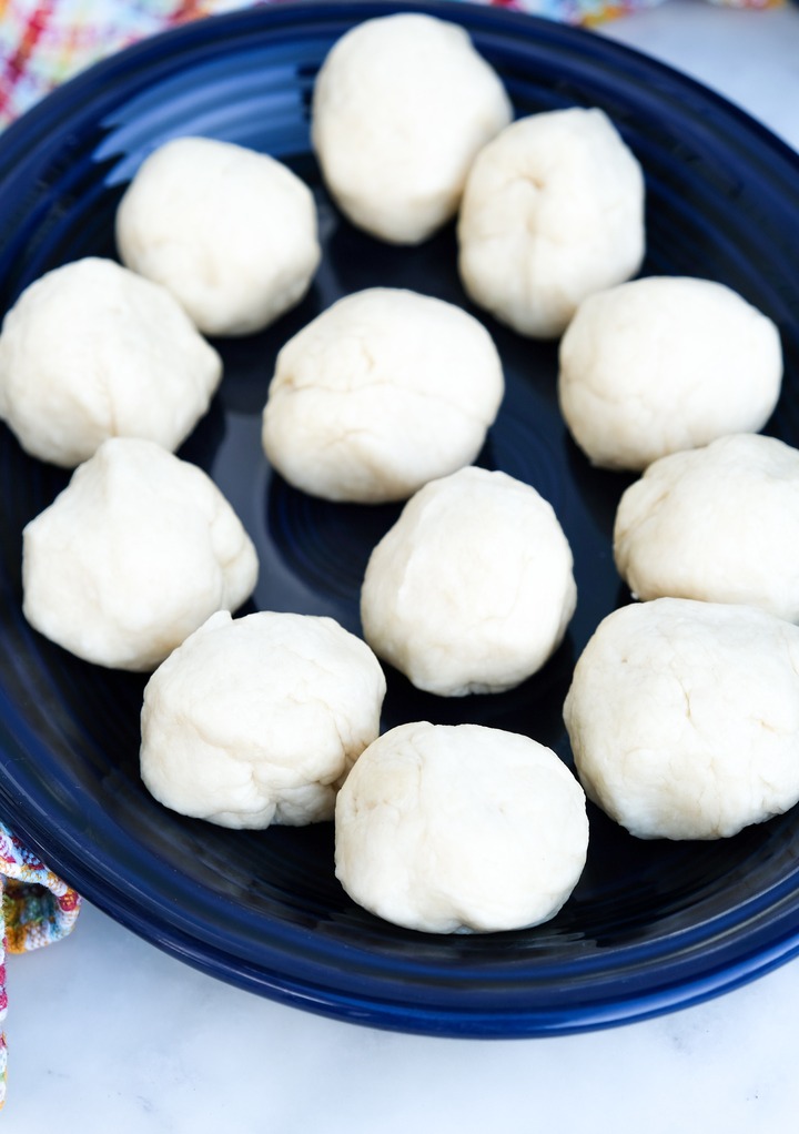 Homemade tortilla dough on a blue serving dish before rolling them in circles to cook. 