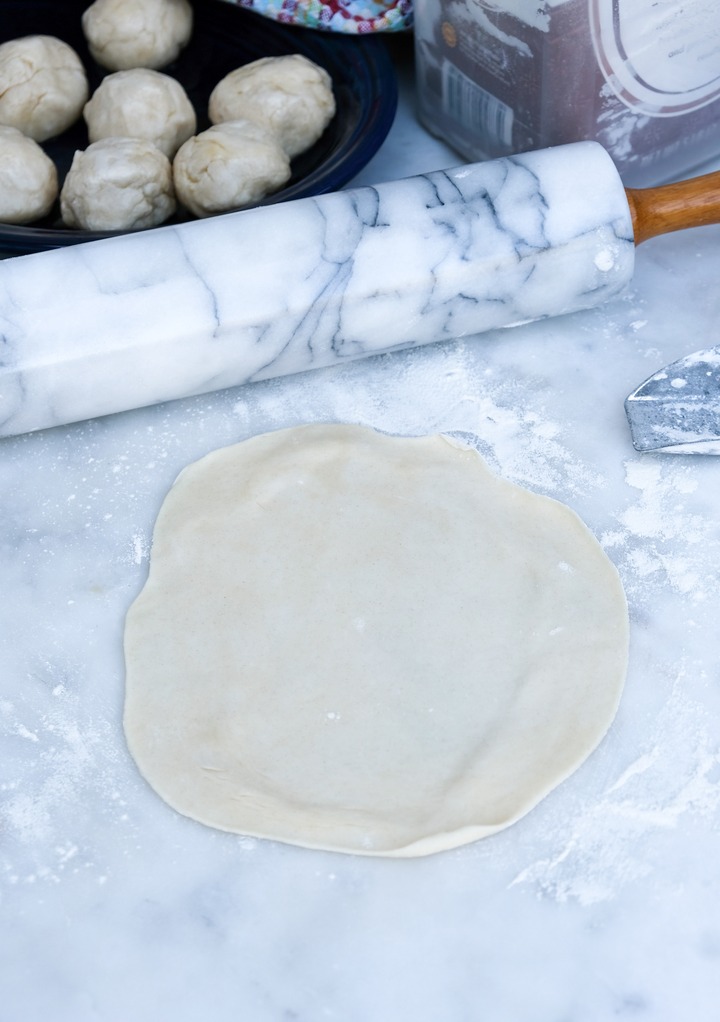 Homemade tortilla dough rolled into a circle with a rolling pin. 