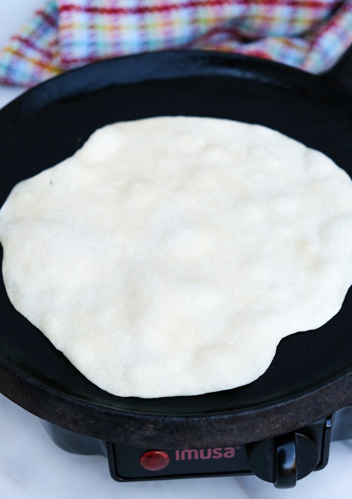 Cooking a tortilla on a iron skillet. 