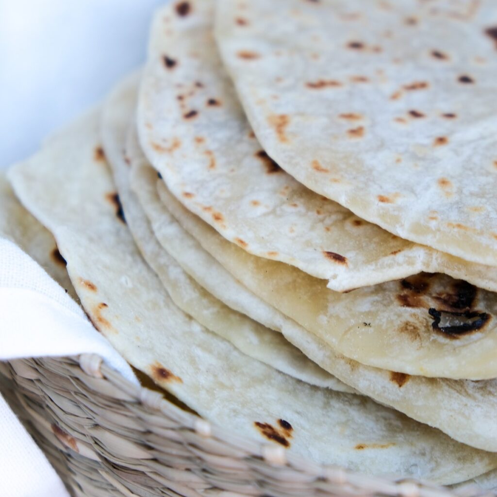A stack of homemade tortillas made without lard in a basket with a kitchen towel.
