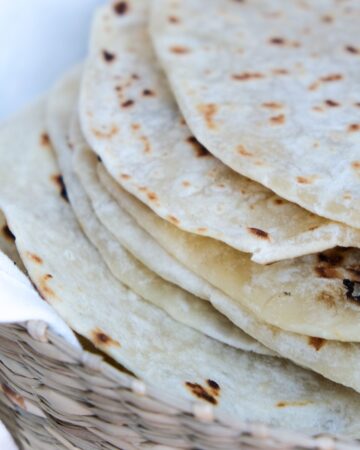 A stack of homemade tortillas made without lard in a basket with a kitchen towel.