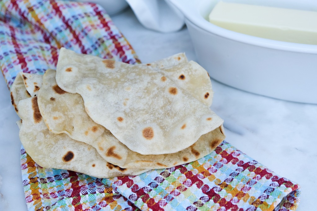 Homemade tortillas recipe without lard on a colorful kitchen towel with butter on the side ready to eat. 