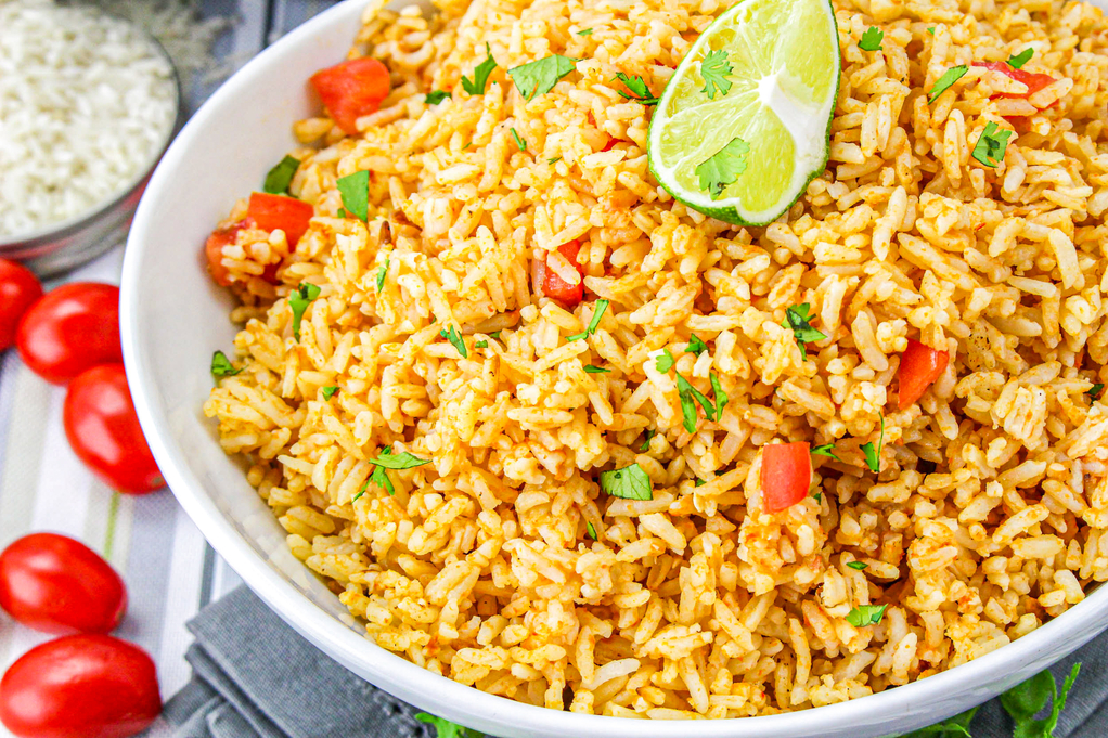 Spanish rice in a serving dish with fresh tomatoes on the side. 