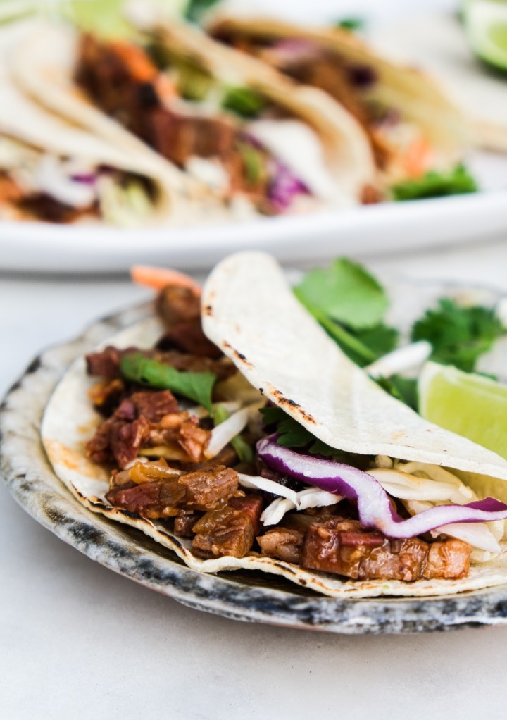 Beef brisket tacos on a tan plate ready to eat. 