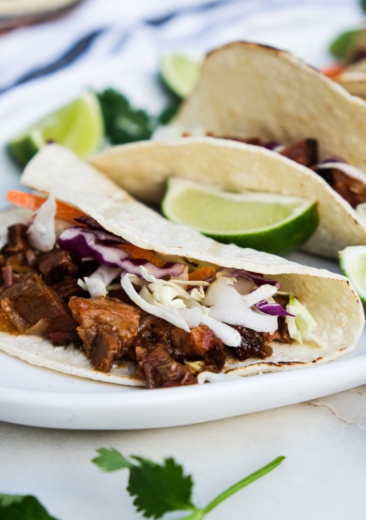 Brisket tacos in a corn tortilla with coleslaw on a white platter.