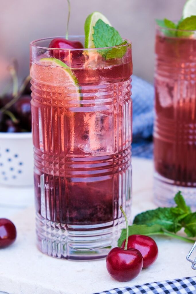 Cherry mojito in a clear glass jar with lime and fresh cherries.