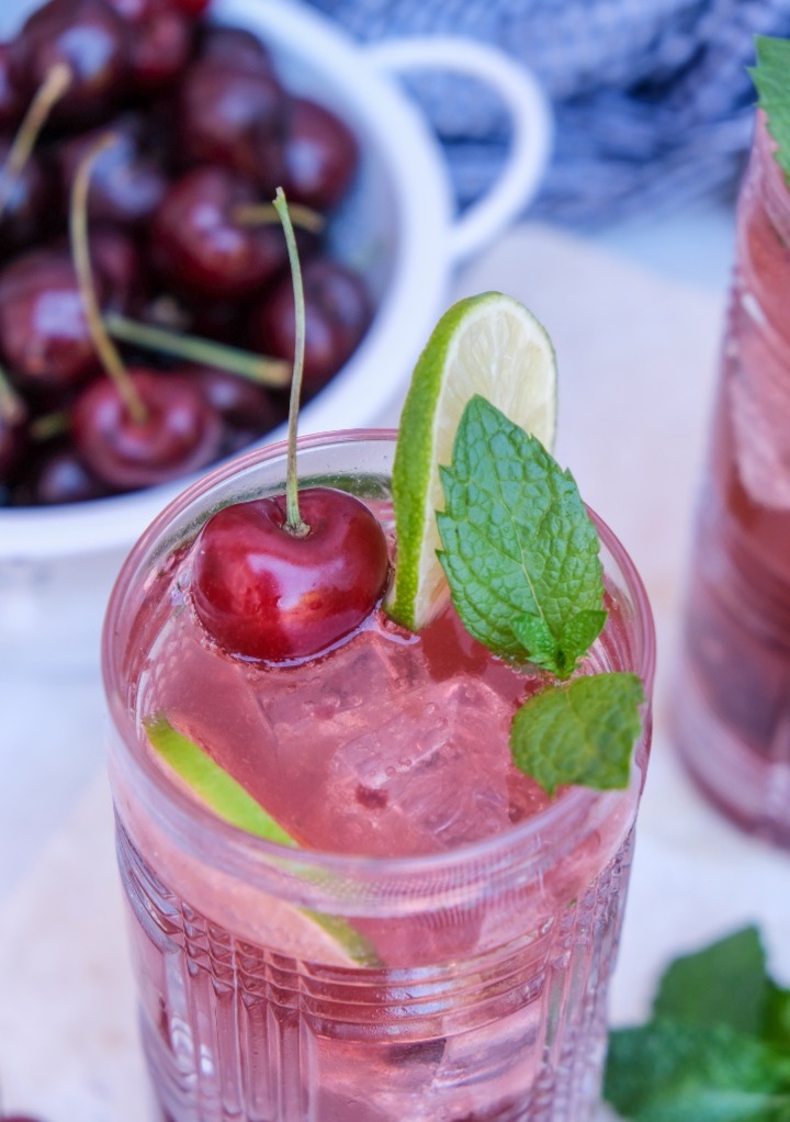 Cherry mojito cocktail in a clear glass topped with mint leaves, lime and a fresh cherry. 