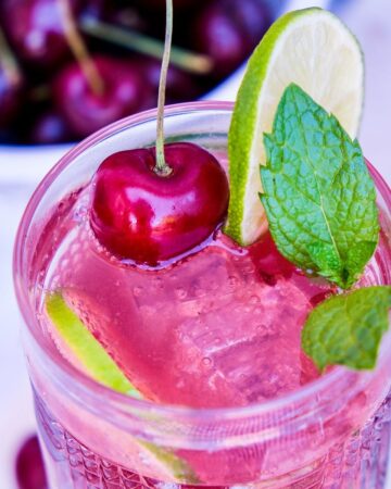 Homemade cherry mojito with lime and fresh cherry juice in a tall cocktail glass.