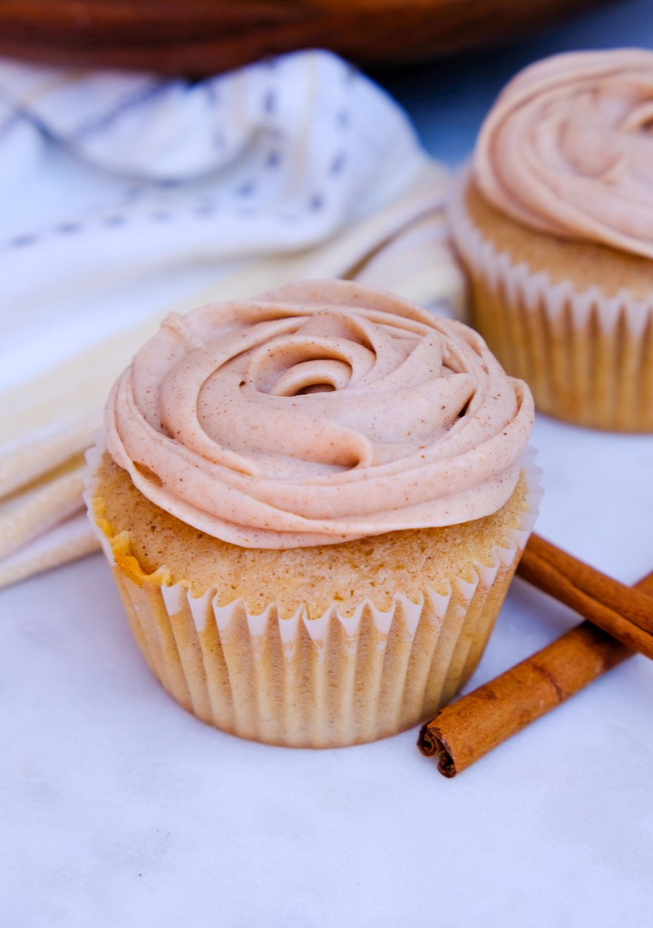 Cupcake with cinnamon cream cheese frosting with cinnamon sticks on the side. 