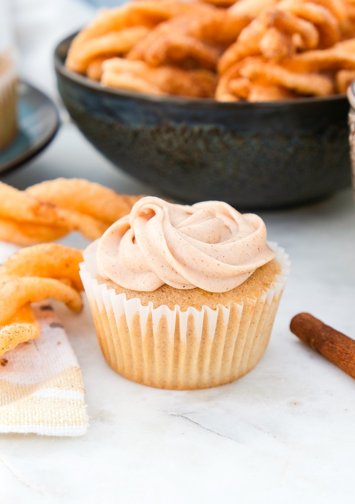 Churro cupcake with a bowl of cinnamon twists in the background in a black bowl.