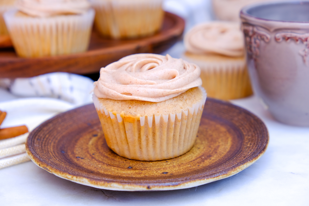 Cinnamon churro cupcake on a brown plate with more cupcakes in the background. 