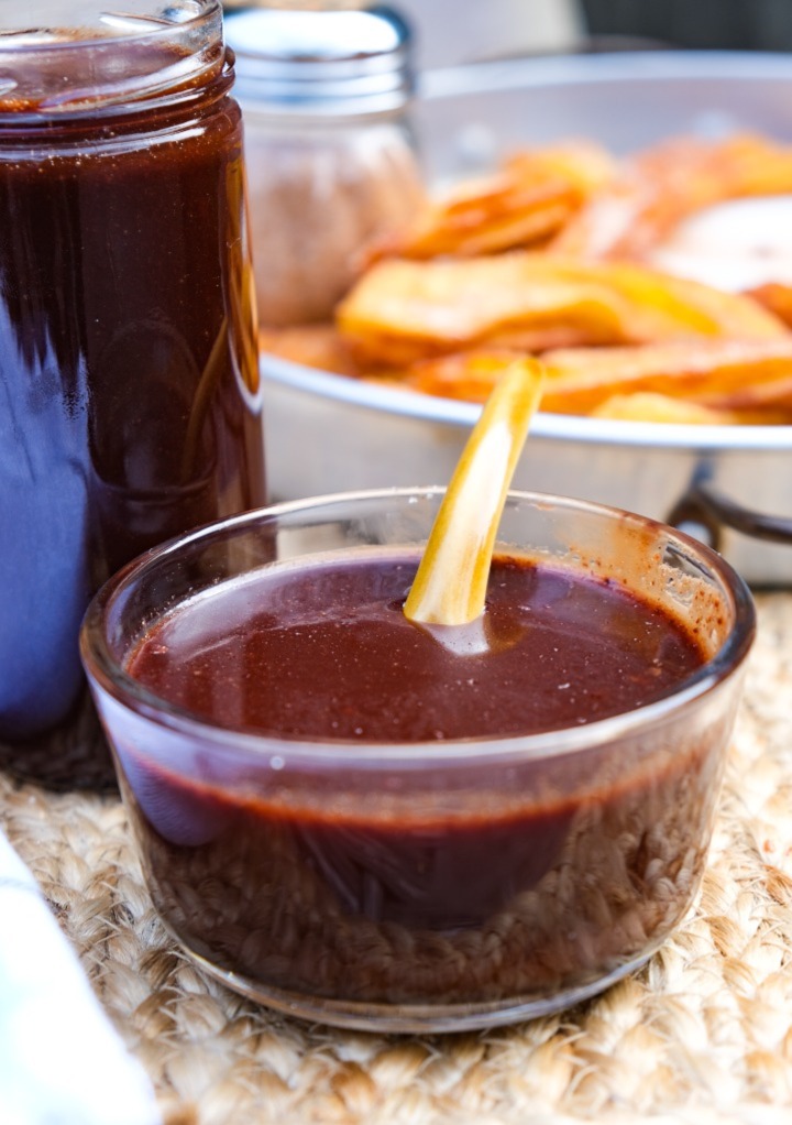 Homemade Ghirardelli chocolate sauce in a small bowl with churros in the background. 