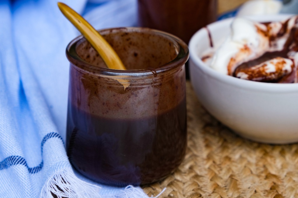 Chocolate sauce with a bowl of vanilla ice cream in the back.