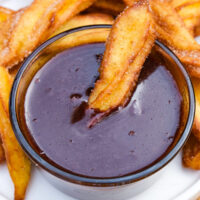 Homemade Ghirardelli chocolate sauce in a small clear serving bowl with a churro dipped in the center.