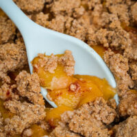 Keto peach crumble with a light blue spoon scooping a portion out to eat.