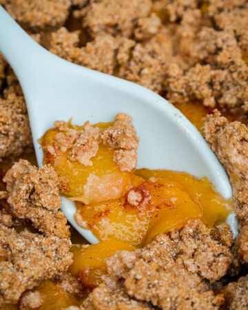 Keto peach crumble with a light blue spoon scooping a portion out to eat.
