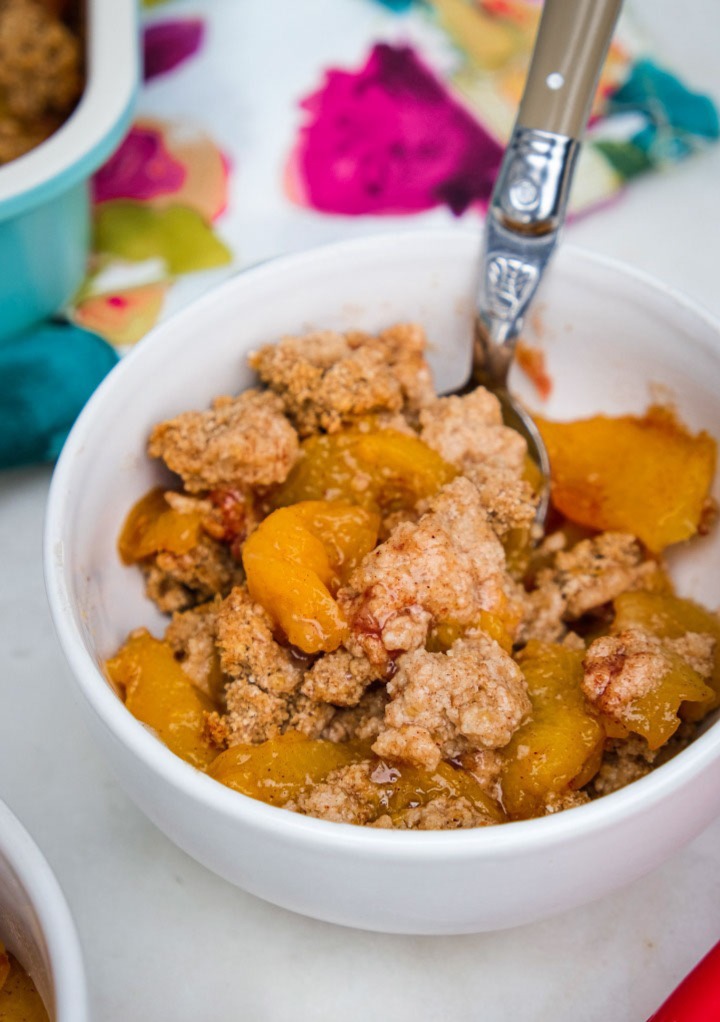 Low carb peach crumble with peaches in a small white serving bowl. 