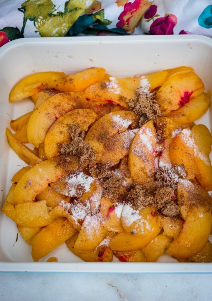 Sliced peaches in a small casserole dish with cinnamon spices on top ready to bake. 