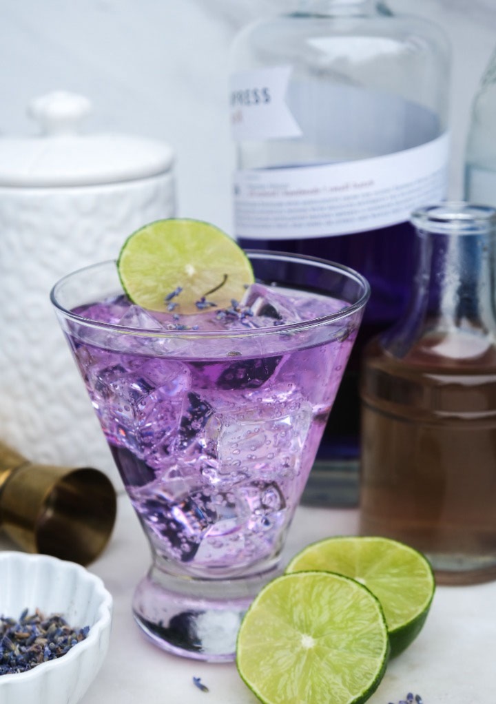 Lavender gin cocktail in a small clear glass with lime slices. 
