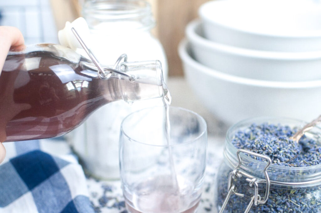 Pouring homemade lavender syrup into a clear glass to make a beverage.