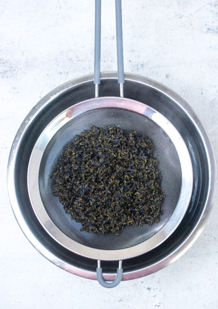 Straining lavender buds using a mesh strainer over a bowl.